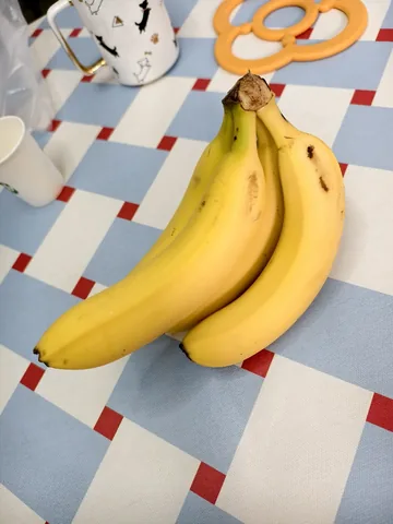 A bunch of bananas shot on a phone, on a checkered tablecloth among clutter