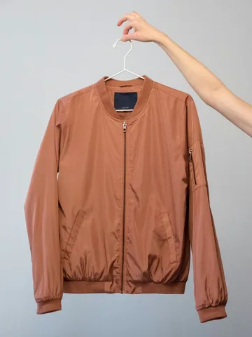 Brown bomber jacket on a hanger, shot on a phone in flat indoor light