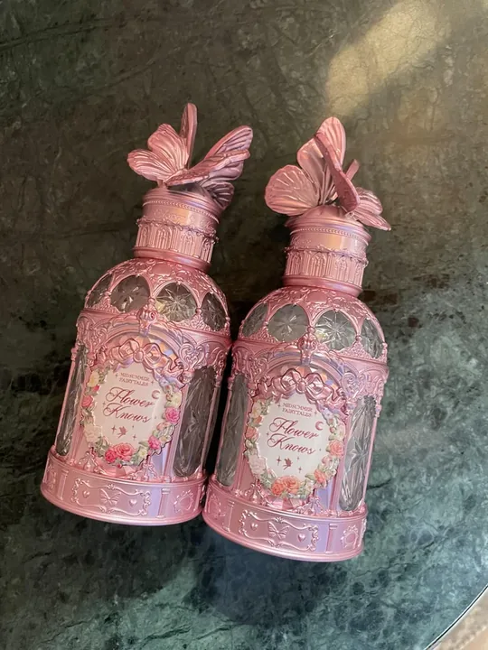 Two Flower Knows perfume bottles shot on a phone on a dark marble surface in warm light