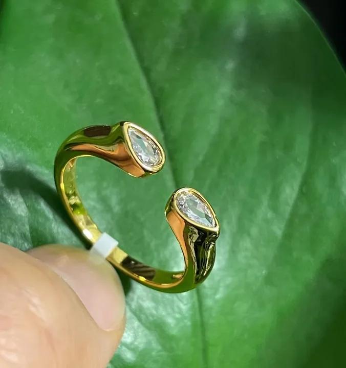 Gold open ring with two pear stones held in fingers over a green leaf, shot on a phone