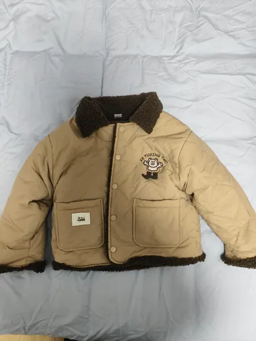 Kids quilted jacket shot on a phone, laid flat on a bed in soft indoor light