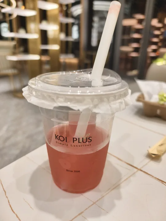 A KOI PLUS pink fruit tea in a clear cup with a straw, shot on a phone on a café table