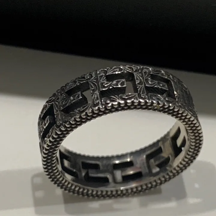 Intricate silver band ring shot on a phone against a dark surface