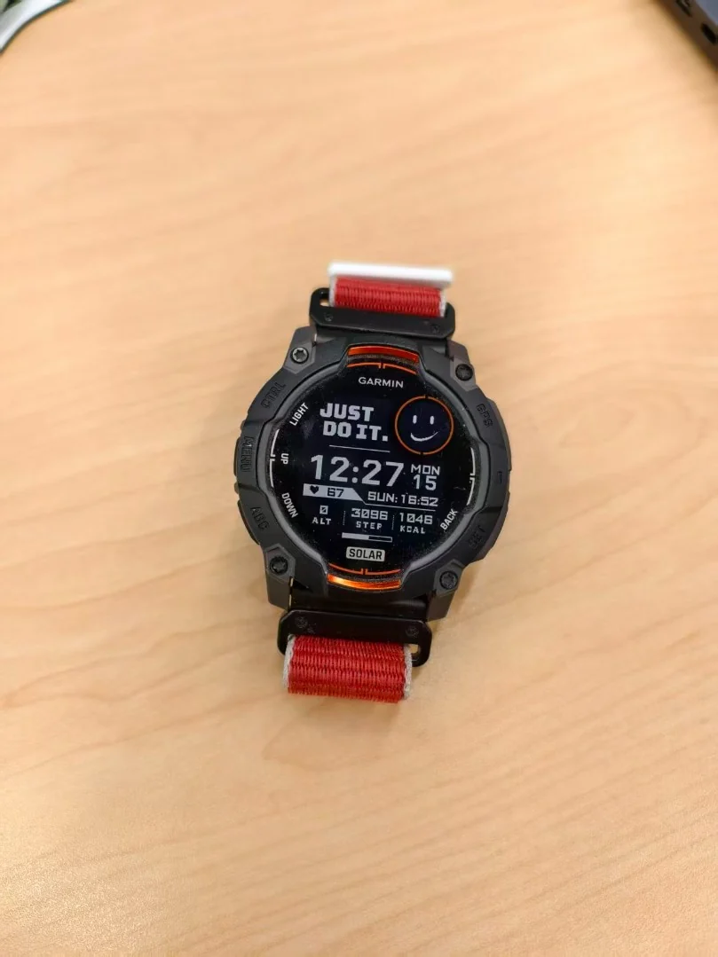 Smartwatch with a digital display and red strap shot on a phone on a wooden surface