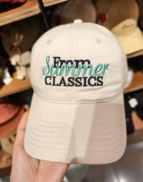 Cream embroidered dad cap held in hand in a shop, shot on a phone against a shelf of other hats
