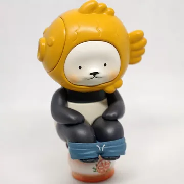A fish-hat vinyl figure shot on a phone, on a grey surface