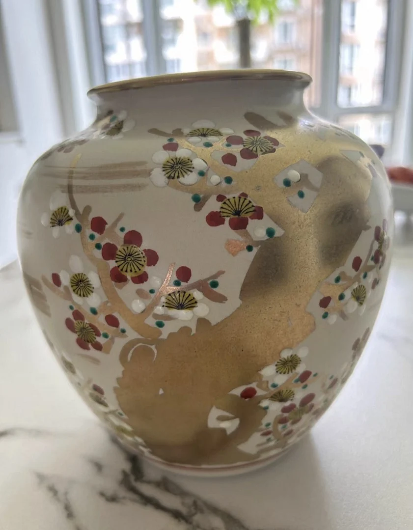 Decorative ceramic vase shot on a phone near a bright window, with reflections and background clutter visible