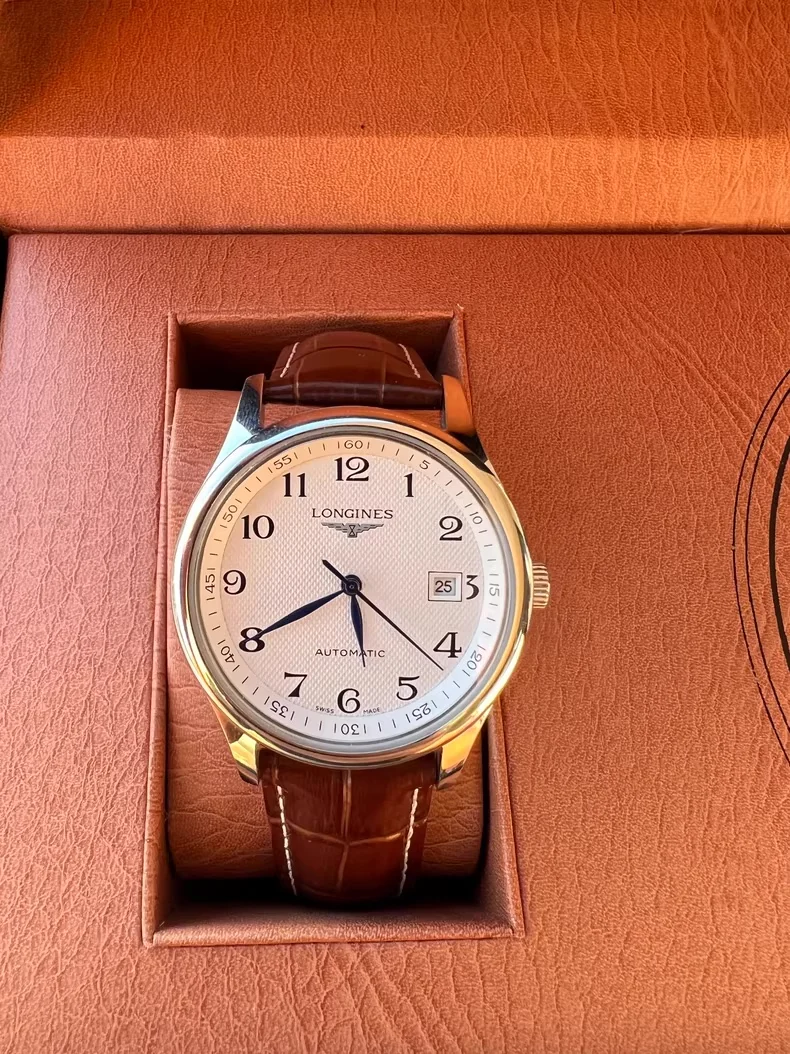 Leather-strap analog watch shot on a phone inside its presentation box in warm indoor light